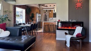 A modern living room with a fireplace, a dining area, and a kitchen in the background. - GSH202-Green Sweet Home-Cozy house in OC (Midway City)