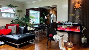 A modern living room with a black leather sofa, a dining area with a glass table, and a kitchen visible through an open door. - GSH202-Green Sweet Home-Cozy house in OC (Midway City)