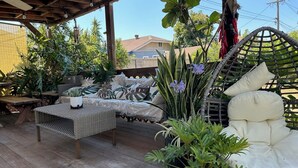 A covered patio with wicker furniture, including a sofa and a table, surrounded by various potted plants. - GSH202-Green Sweet Home-Cozy house in OC (Midway City)
