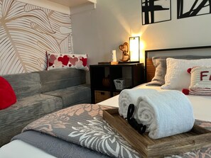 Ein ordentlich eingerichtetes Hotelzimmer mit Bett, Holz-Nachttisch, Beistelltisch und einer Couch.