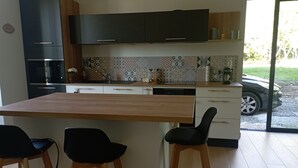A modern kitchen with a wooden island, bar stools, and a view of a parked car outside. - Renovated 1920s house, 15 minutes' walk from town center, quiet location. (Aurillac)