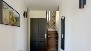 A hallway with a checkered floor, a wooden bench, a black door, and a staircase with a leaf-patterned wall. - Renovated 1920s house, 15 minutes' walk from town center, quiet location. (Aurillac)