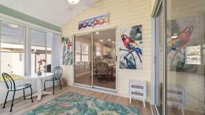 A room with a sliding glass door, a dining area with chairs and a table, and tropical-themed artwork on the walls. - The Villages! 2 Squares!-Pool access -Free Wifi-All Amenities-Shopping galore! (Lady Lake)