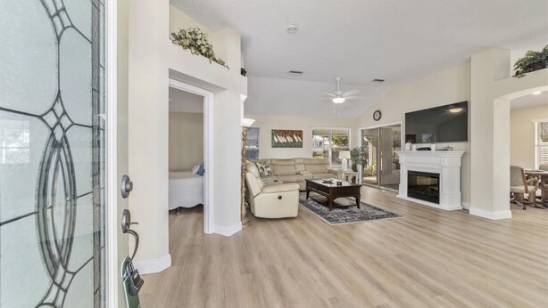 A spacious living room with a fireplace, a sofa, a coffee table, and a TV mounted on the wall. - The Villages! 2 Squares!-Pool access -Free Wifi-All Amenities-Shopping galore! (Lady Lake)