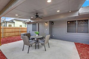 Une terrasse extérieure avec une table ronde et des chaises, un ventilateur de plafond et une vue sur les maisons voisines.