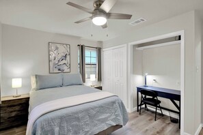 Une chambre à coucher avec un lit, un bureau, un ventilateur de plafond et une fenêtre avec des stores.