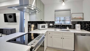 Une cuisine moderne avec des meubles blancs, un dosseret carrelé noir et blanc, un four à micro-ondes encastré, un lave-vaisselle en acier inoxydable et une plaque de cuisson à induction noire.