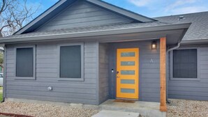 Une maison de plain-pied à l’extérieur gris, avec une porte d’entrée jaune dotée d’une fenêtre et un petit porche.