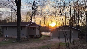 A two-story house with a garage, surrounded by trees and a body of water. - Fall is beautiful on Mystery Lake! Book now for fishing, campfires and boating! (Spooner)