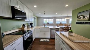 A modern kitchen with white cabinets, a stainless steel range hood, and a wooden countertop.