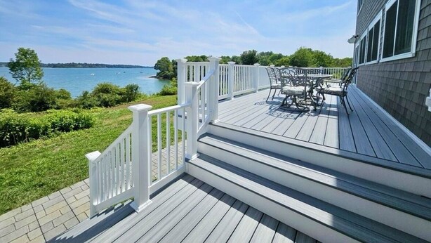 A wooden deck with a white railing, a table with chairs, and a view of the water.