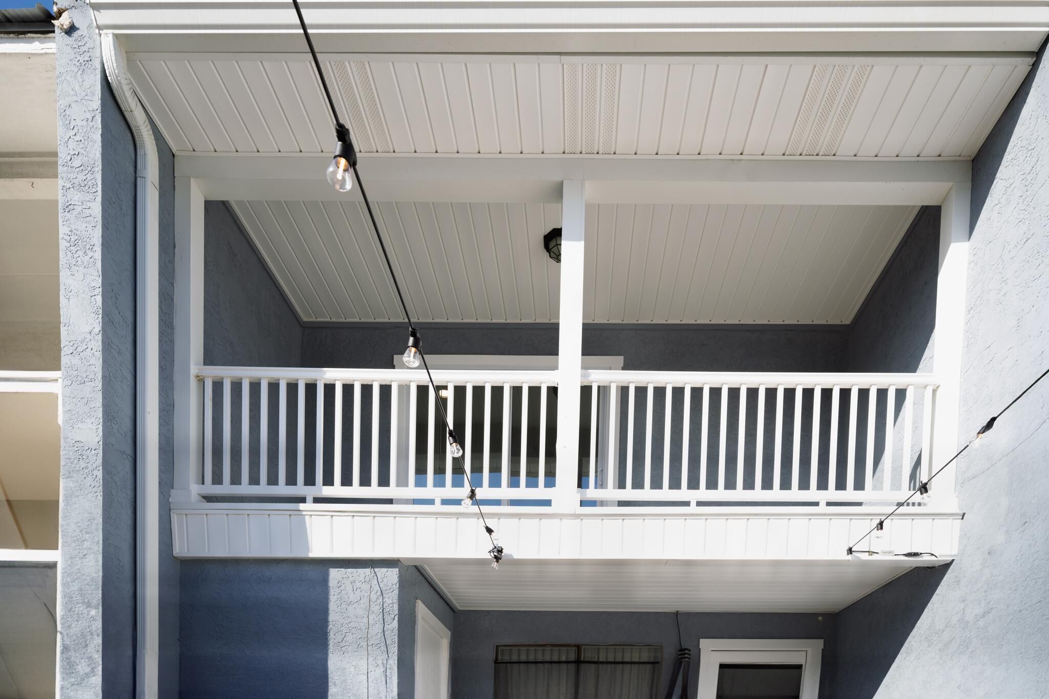 A two-story building with a balcony on the upper floor, featuring a white railing and a hanging light fixture.