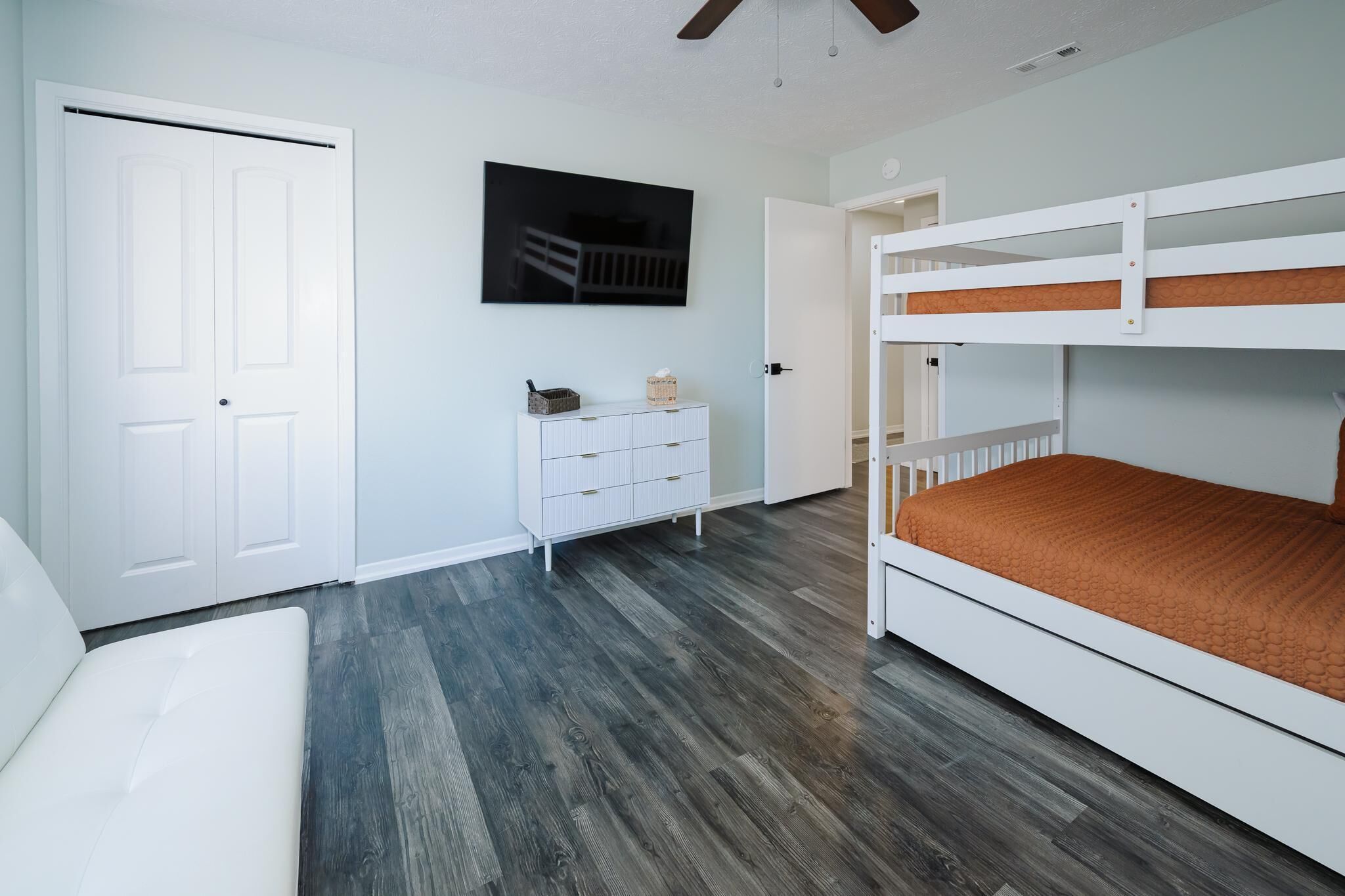 Ein Schlafzimmer mit einem Etagenbett, einer weißen Kommode, einer Tür und einem Deckenventilator.