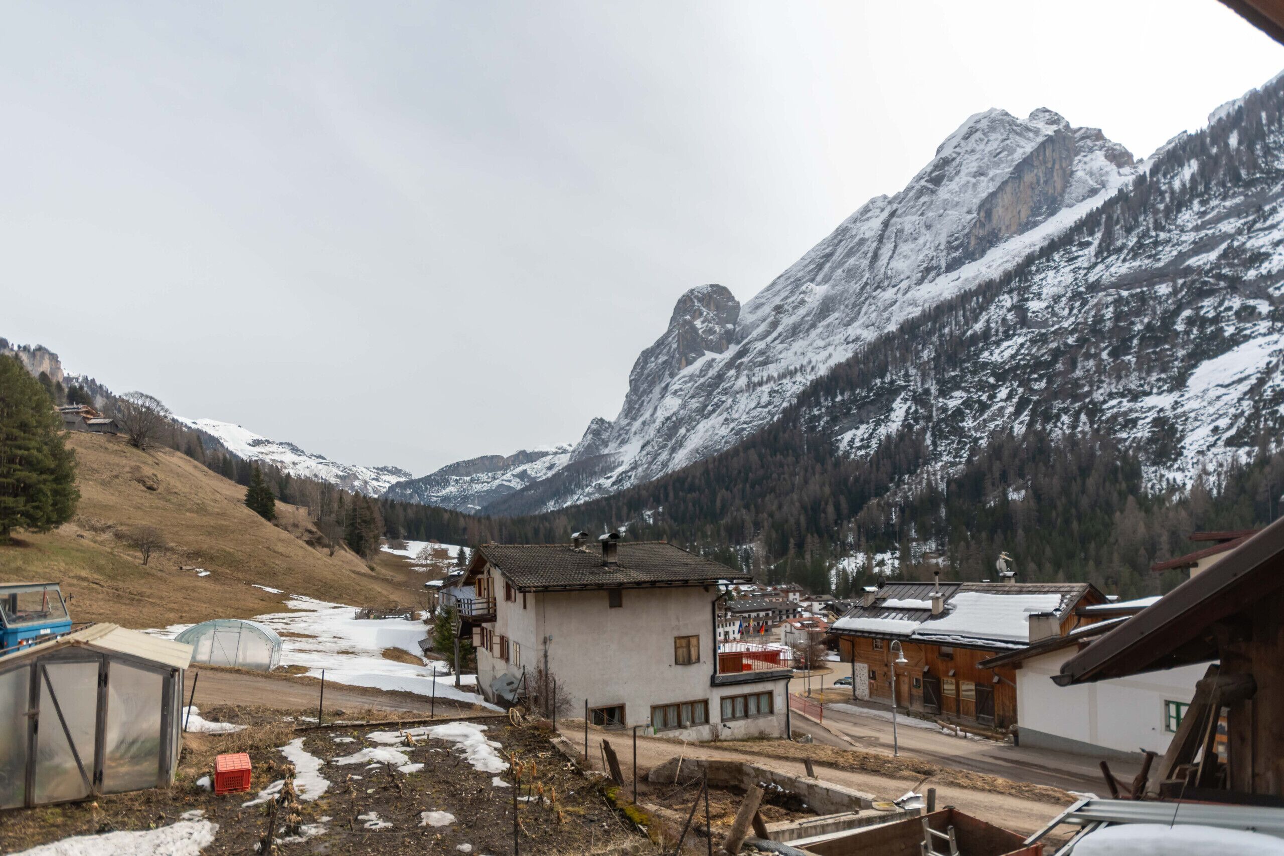 A mountain village with traditional buildings, a greenhouse, and a small pond.