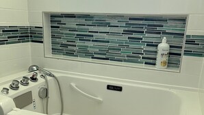 Un baño con bañera, ducha y ventana con salpicadero de azulejos.