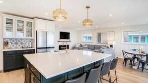 A modern kitchen with a large island, dark cabinets, and a dining area with a wooden table and chairs. - Lakefront 3-bedroom cottage on Sand Point with AC, WiFi, King bed, Firepit (Pigeon)