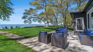 A patio area with wicker furniture and a view of the lake. - Lakefront 3-bedroom cottage on Sand Point with AC, WiFi, King bed, Firepit (Pigeon)