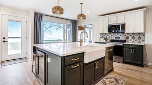 A modern kitchen with dark cabinetry, a large island, and pendant lighting. - Lakefront 3-bedroom cottage on Sand Point with AC, WiFi, King bed, Firepit (Pigeon)