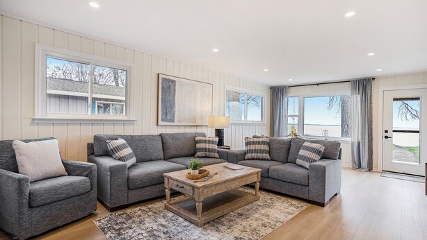 A modern living room with two grey sofas, a wooden coffee table, and a large window with curtains. - Lakefront 3-bedroom cottage on Sand Point with AC, WiFi, King bed, Firepit (Pigeon)