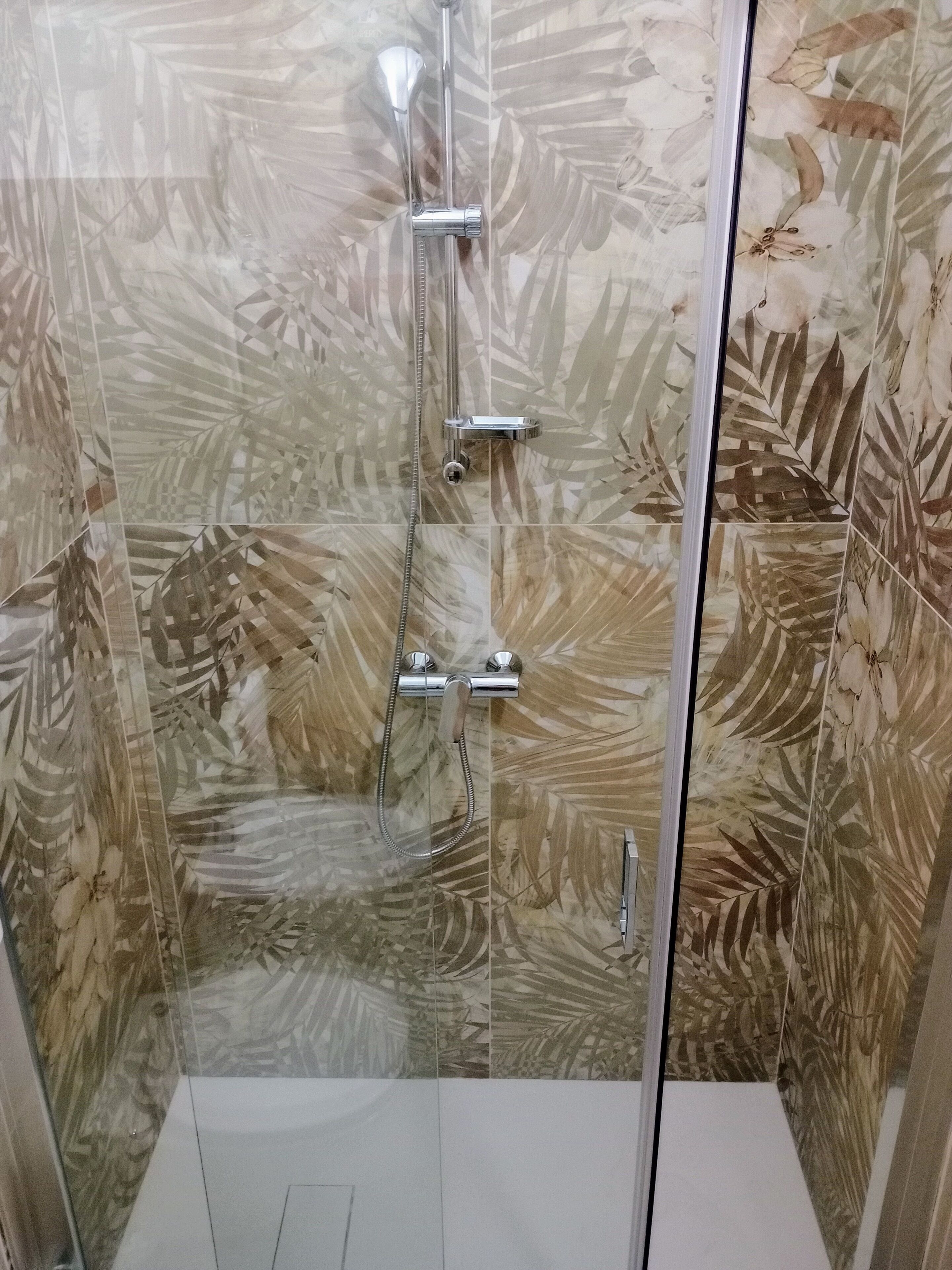 Eine Dusche mit Glastür, Handbrause und am Wand montiertem Wasserhahn.