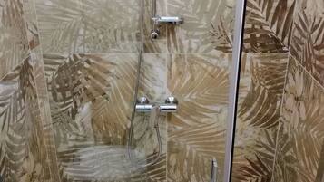 Eine Dusche mit Glastür, Handbrause und am Wand montiertem Wasserhahn.