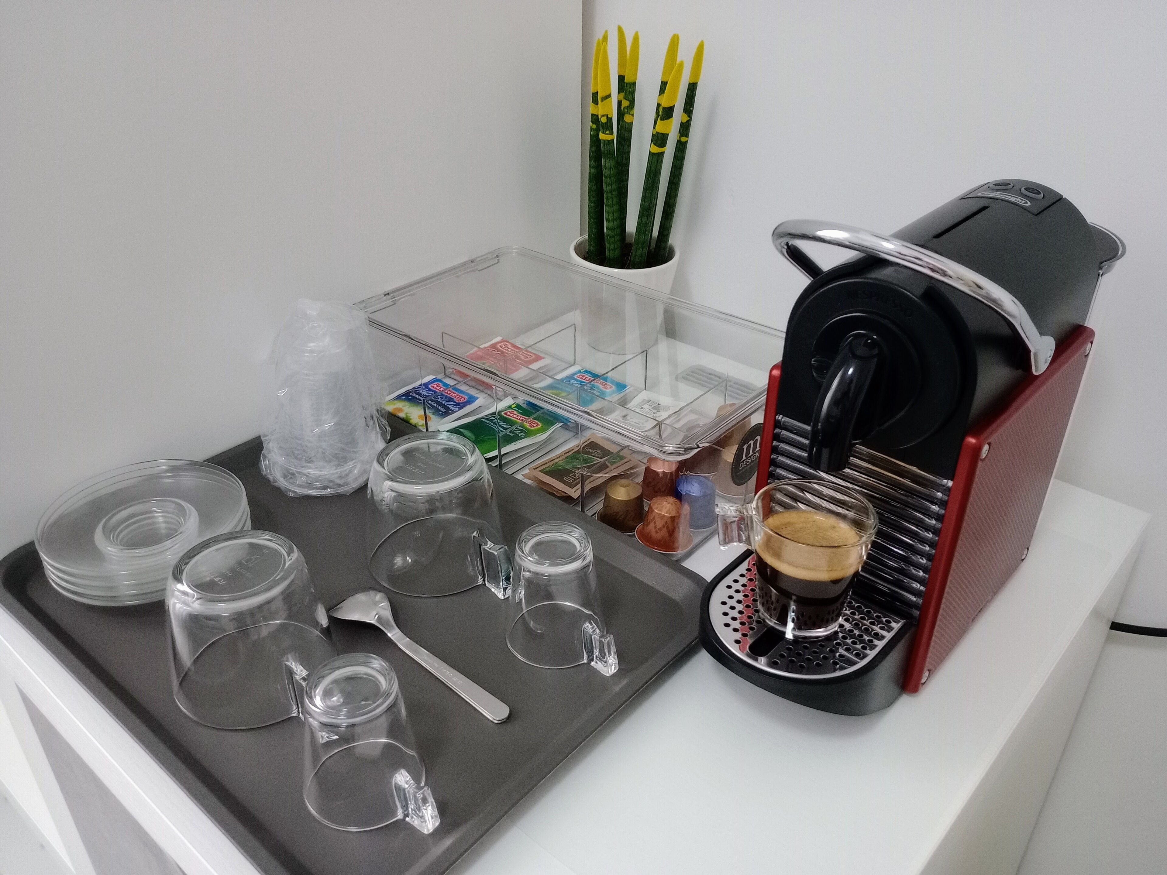 Kaffestation med kaffemaskine, kopper og bakke med bestik.