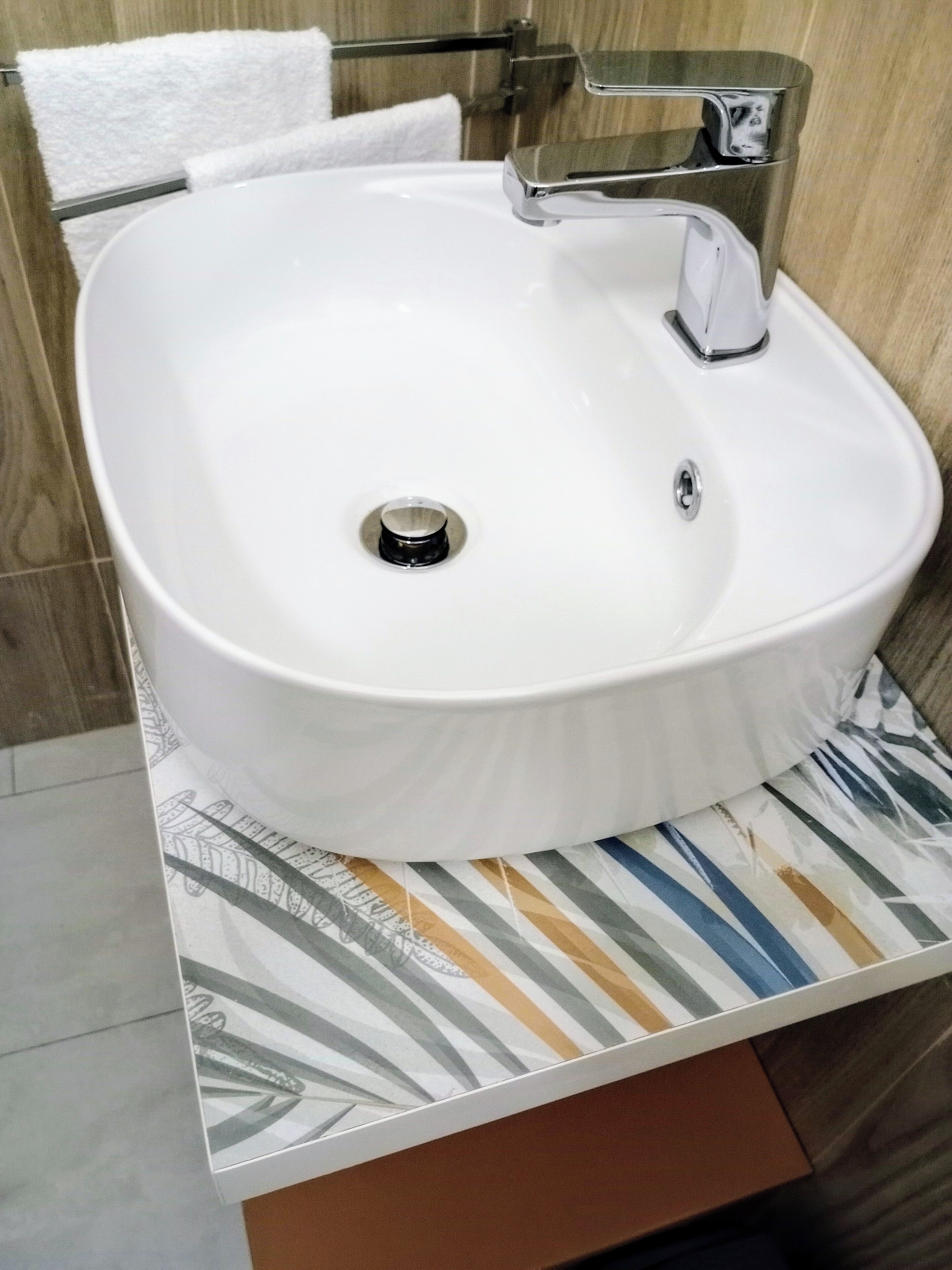 Un baño con lavamanos blanco, grifo cromado y un perchero para toallas.