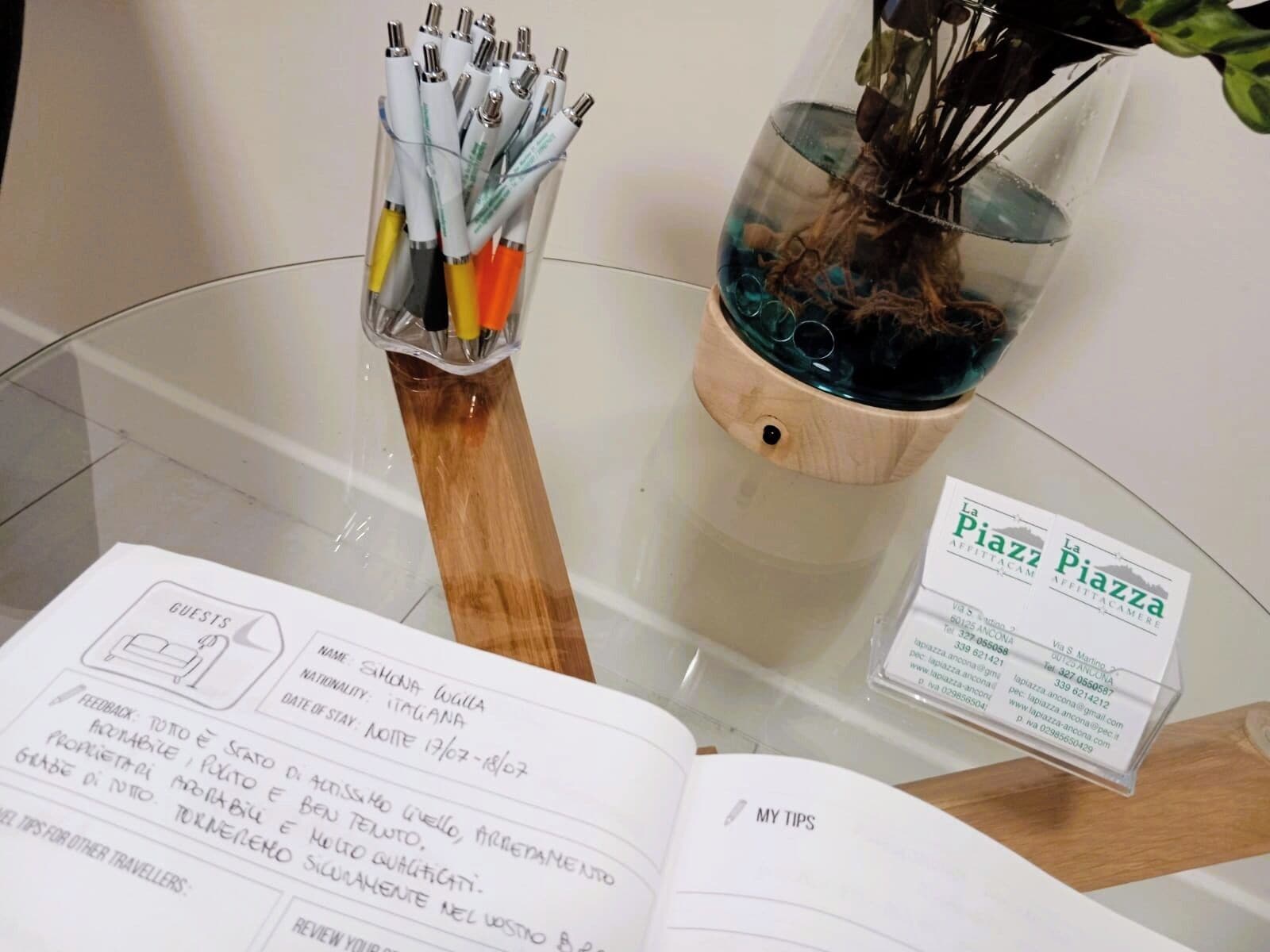 A glass table with a notebook, a pen holder, and a glass vase with a plant.