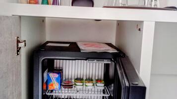 Un refrigerador compacto con dispensador de leche y jugo, una cafetera y un pequeño estante con objetos decorativos.