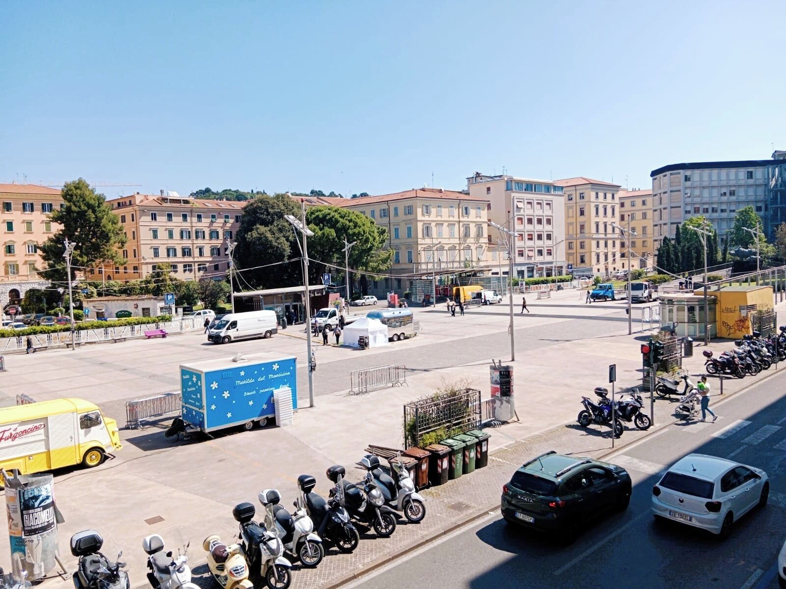 A busy urban street with parked scooters, cars, and a blue truck.