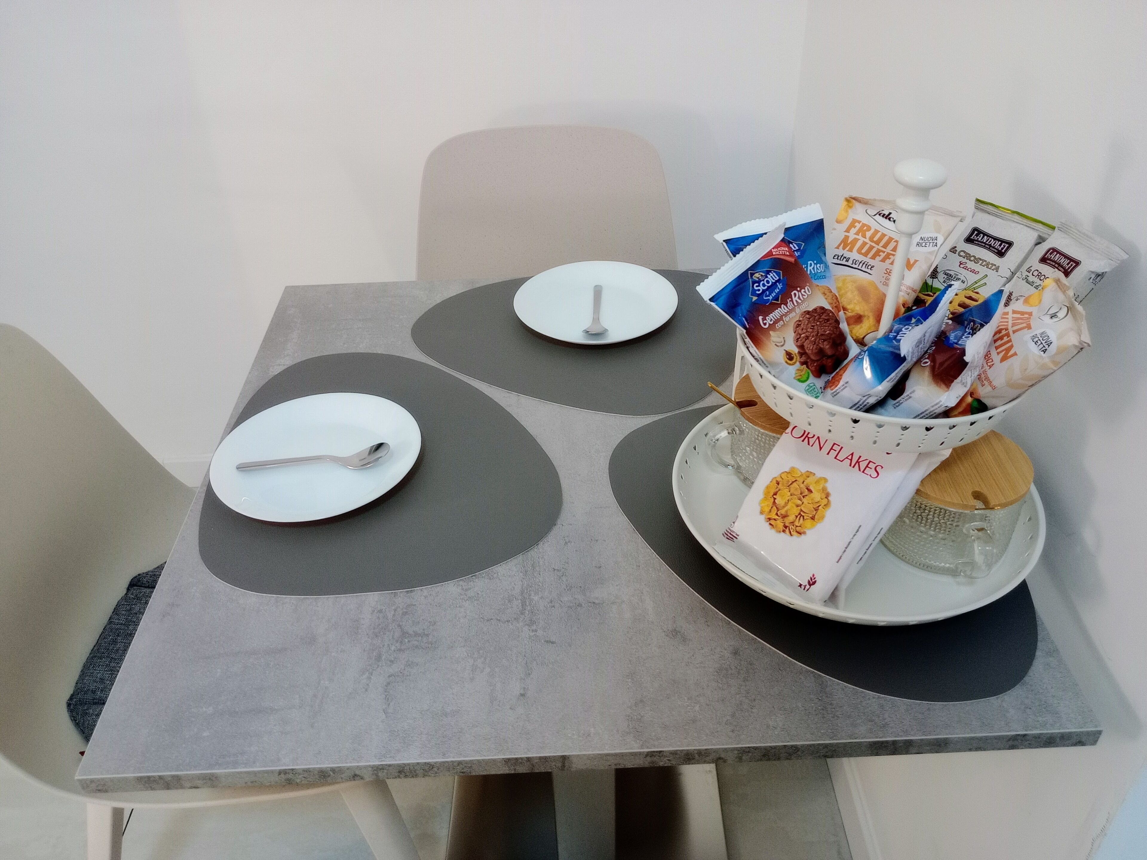 A table with two plates, a spoon, and a basket containing cereal boxes.