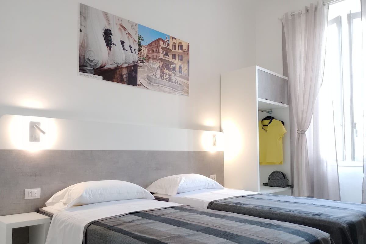 Quarto de hotel com duas camas, um guarda-roupa e um quadro de uma paisagem urbana.