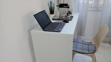 A laptop on a white desk with a coffee machine, a glass of coffee, and a potted plant.