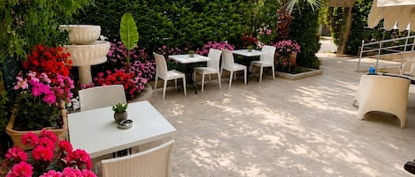 Un patio al aire libre con mesas y sillas, rodeado de exuberante follaje y plantas en flor.