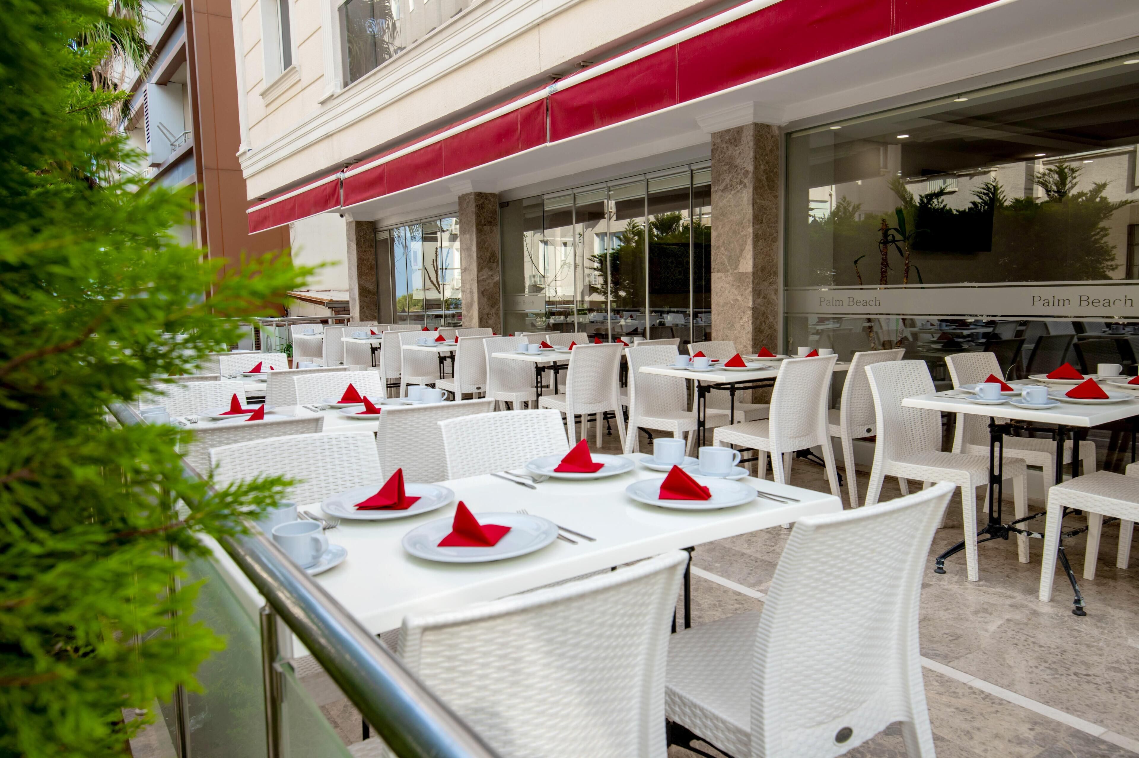 An outdoor dining area with white tables and chairs, red napkins, and a red awning.
