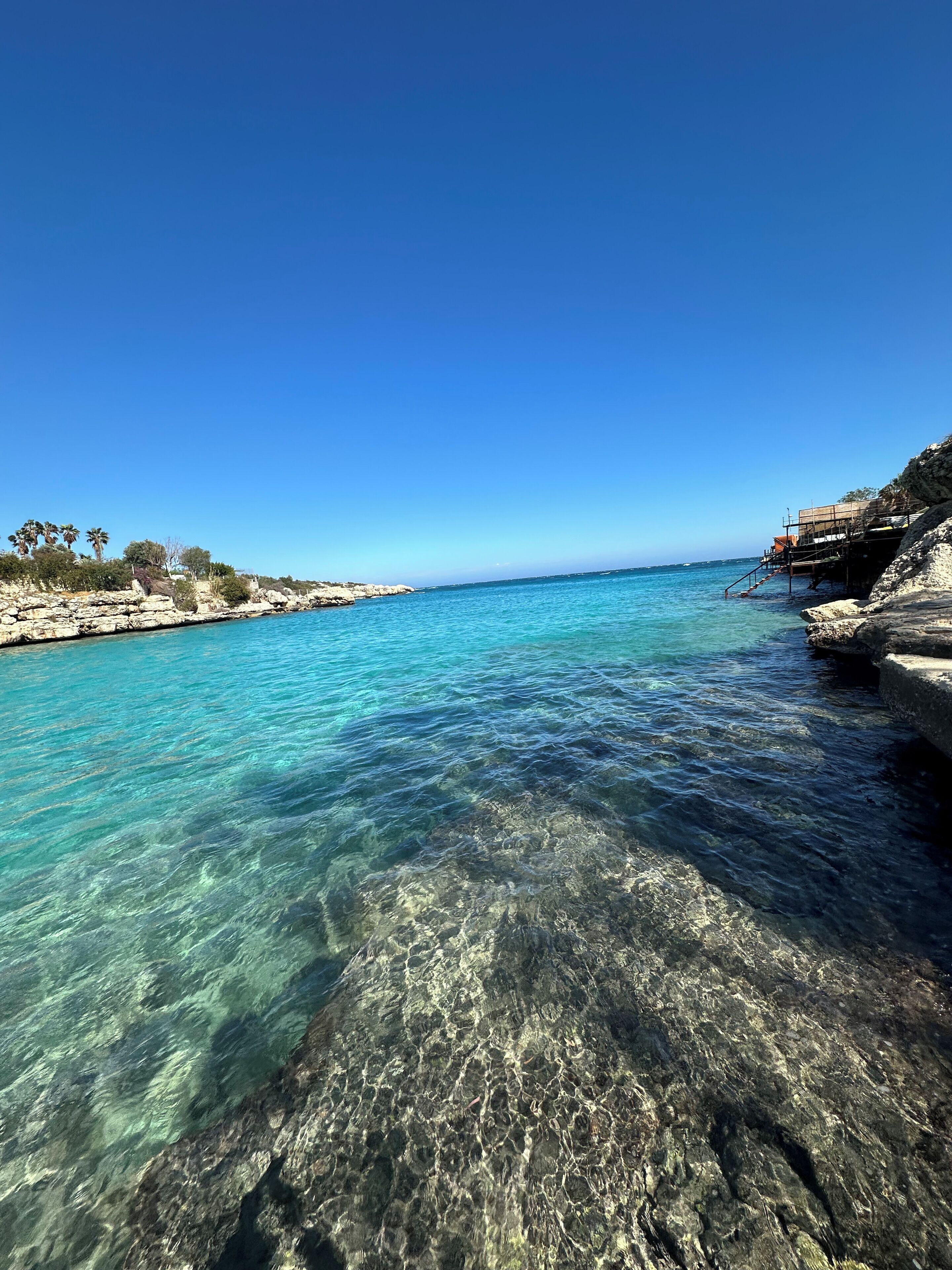 A coastal scene with clear turquoise water, rocky shorelines, and a clear blue sky.