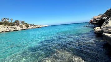 A coastal scene with clear turquoise water, rocky shorelines, and a clear blue sky.