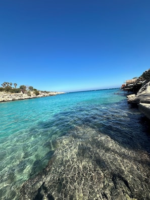 A coastal scene with clear turquoise water, rocky shorelines, and a clear blue sky. - PALM BEACH HOTEL (Silifke)