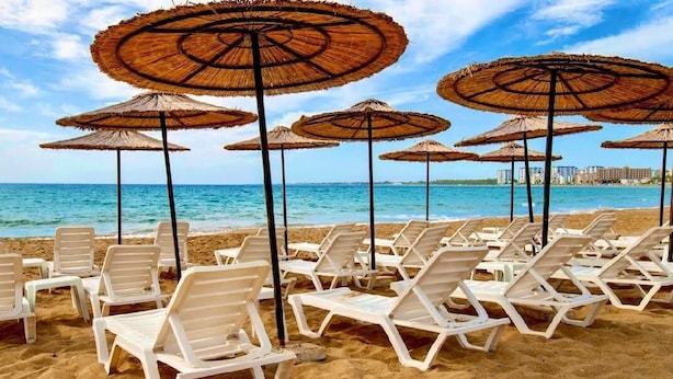 A beach with rows of white lounge chairs and thatched umbrellas. - PALM BEACH HOTEL (Silifke)
