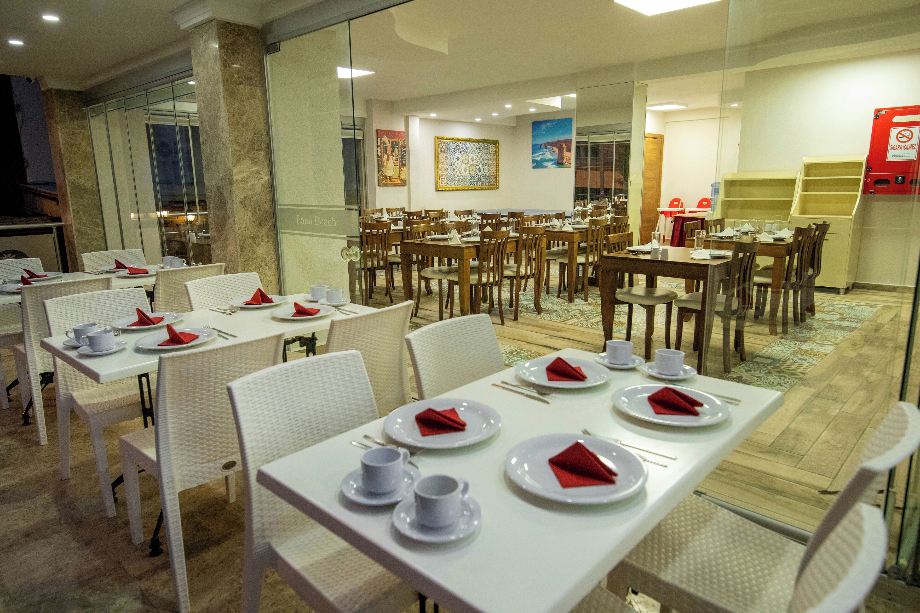 A spacious dining area with multiple tables set for guests, featuring white tablecloths and red napkins.