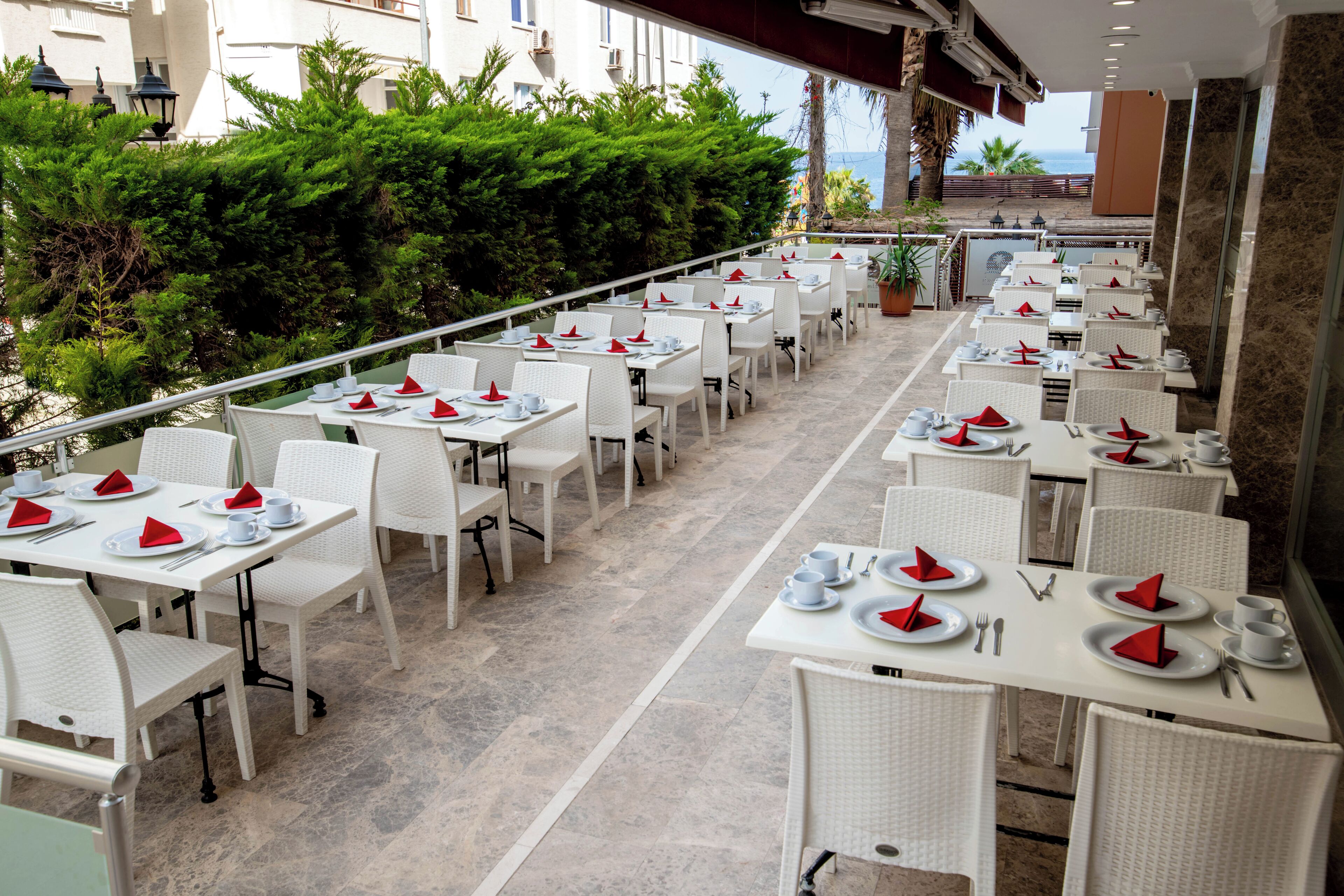 A restaurant with white tables and chairs, red napkins, and a view of the sea.