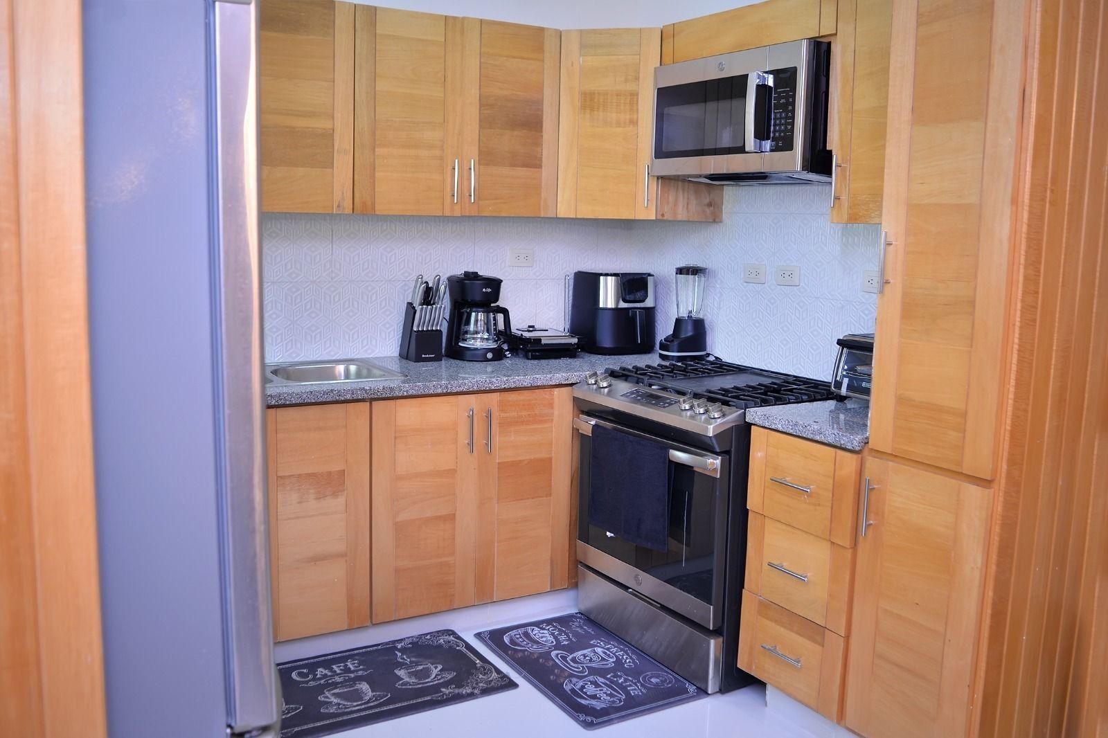 Una cocina compacta con armarios de madera, estufa de acero inoxidable, microondas y cafetera.