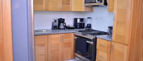 Una cocina compacta con armarios de madera, estufa de acero inoxidable, microondas y cafetera.