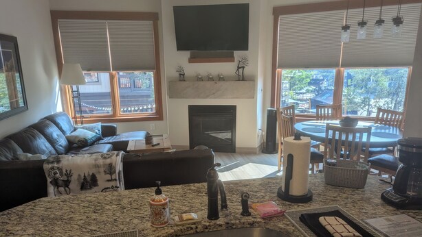 A modern living room with a large granite kitchen island, a fireplace, and a dining area with a view of the outdoors.