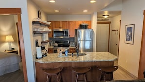 A compact kitchen with a central island, wooden cabinets, stainless steel appliances, and a bar stool seating area.