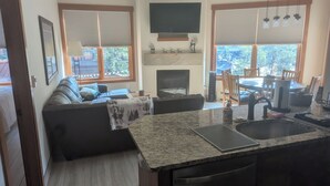 A modern living room with a fireplace, a dining area, and a kitchen with granite countertops.