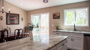 A kitchen with a marble countertop, white cabinets, and a large window with a view of trees. - 3-bedroom house near Deep River, Toyota Megasite, NC Zoo & Zoo Sports Complex (Franklinville)