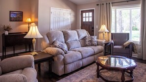 A living room with a sofa, armchairs, a glass coffee table, and lamps. There is a door and a window with curtains. - 3-bedroom house near Deep River, Toyota Megasite, NC Zoo & Zoo Sports Complex (Franklinville)