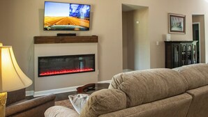 A living room with a flat-screen TV mounted above a fireplace, a sofa, and a lamp. - 3-bedroom house near Deep River, Toyota Megasite, NC Zoo & Zoo Sports Complex (Franklinville)