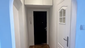 Een gang met een houten visgraatvloer, witte wanden en een witte deur met een raam.